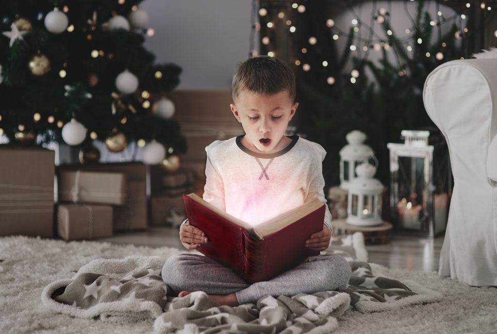 Child reading a holiday-themed book in a cozy nook with festive decorations and soft lighting