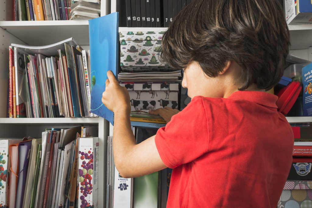 Young child reaching for books on a low shelf designed for easy access and independent reading.