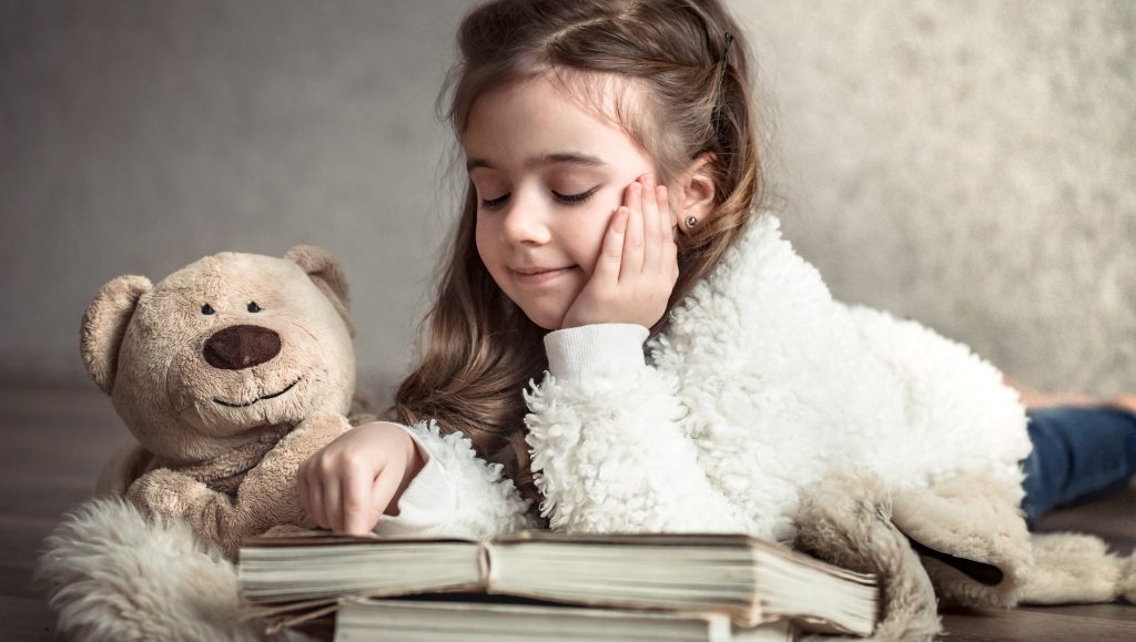 Interactive reading for kids: girl reading a book with a teddy bear during storytime